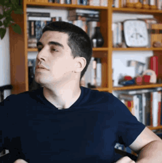 a man in a blue shirt sits in front of a bookcase