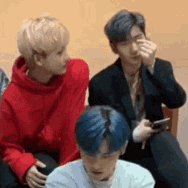 a group of young men are sitting next to each other and one of them is covering his face with his hand .