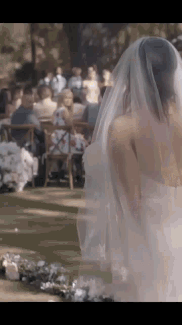a bride in a white dress and veil is walking down the aisle at a wedding .