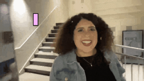 a woman with curly hair is smiling in front of stairs and a sign that says i