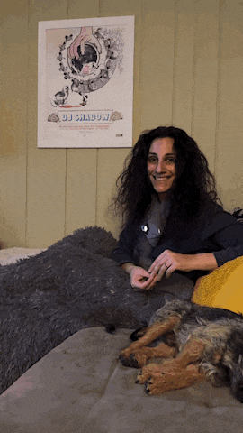 a woman sitting on a couch next to a dog with a dj shadow poster behind her
