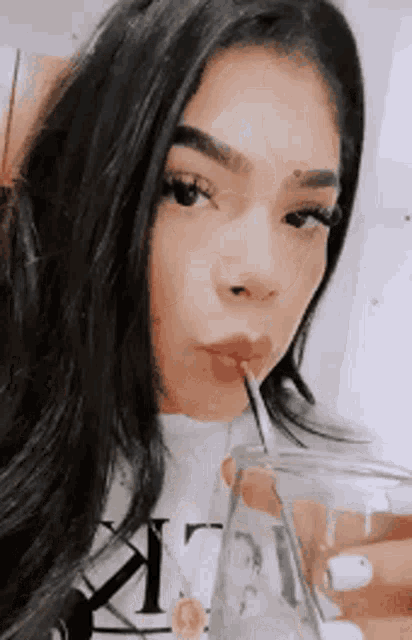 a woman is drinking a glass of water with a straw .