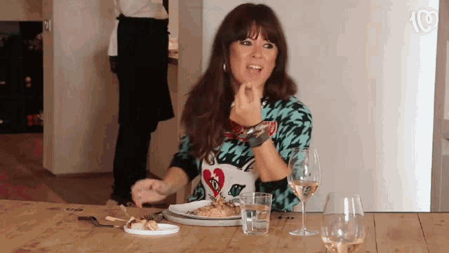 a woman sitting at a table with a plate of food and wine glasses