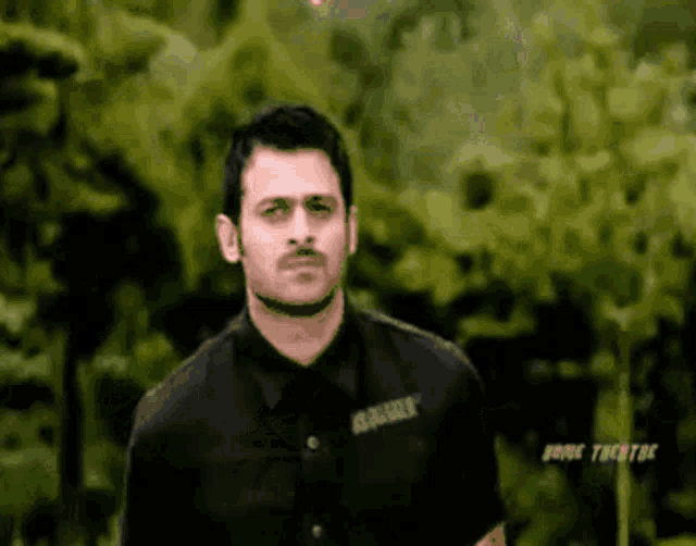 a man in a black shirt is standing in front of some trees .