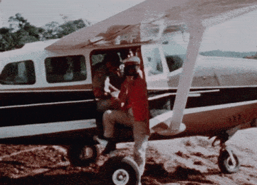 a man in a red shirt is standing in front of a small plane