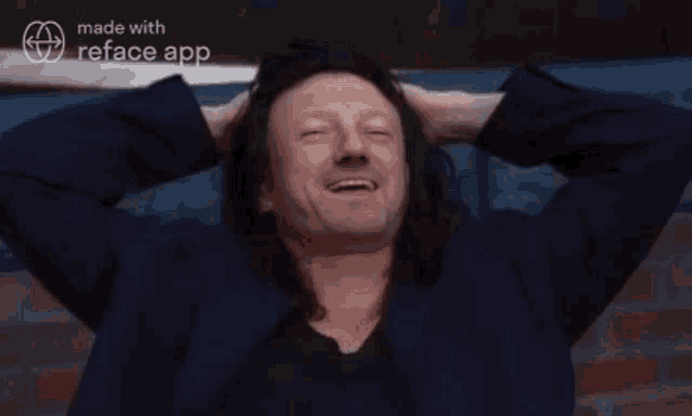 a man with long hair is smiling with his hands behind his head