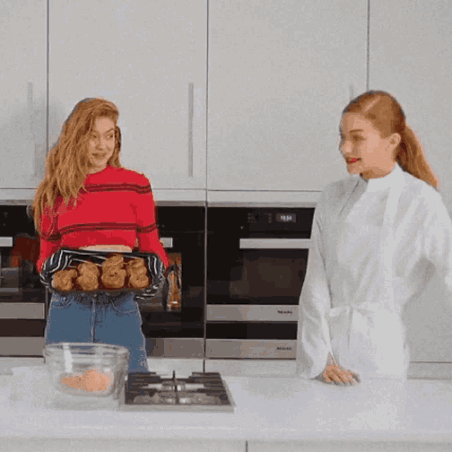 a woman in a red sweater is holding a tray of pastries next to a woman in a white coat