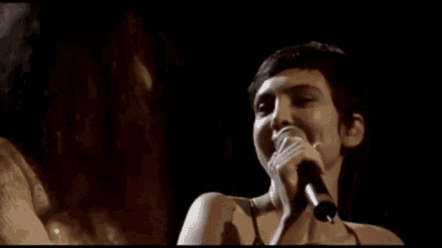 a woman is singing into a microphone in a dark room while another woman smiles in the background .