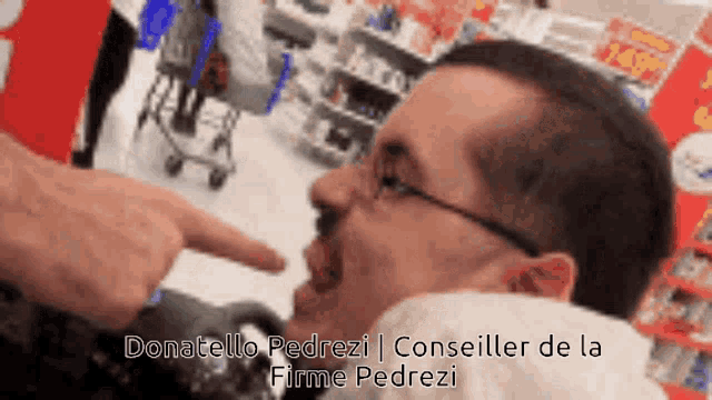 a man with glasses is pointing at another man 's face in a store .