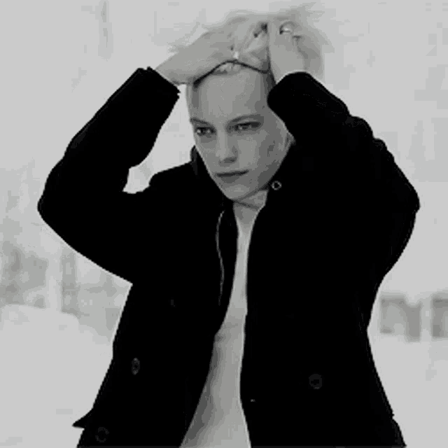 a woman in a black jacket is holding her hair