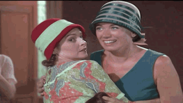 two women wearing hats are hugging and smiling for the camera