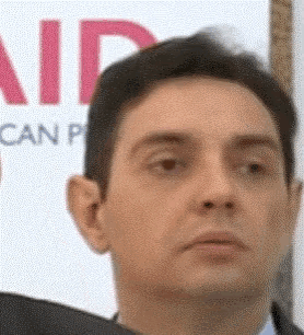 a man in a suit stands in front of a sign that says aid can