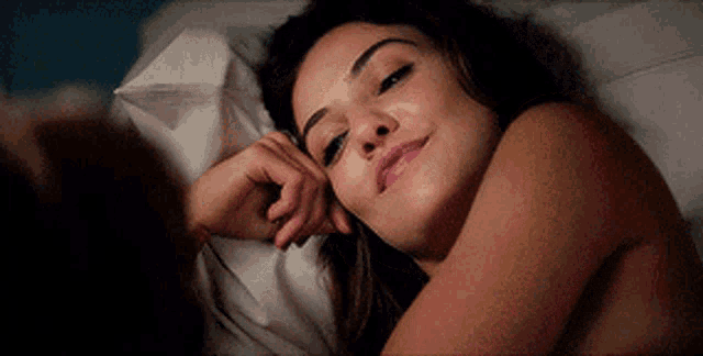 a naked woman is laying in a bed with a white pillow and smiling .