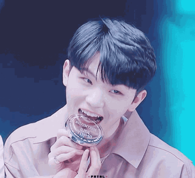 a young man is holding a plaque that says seventeen global top 10 in his mouth