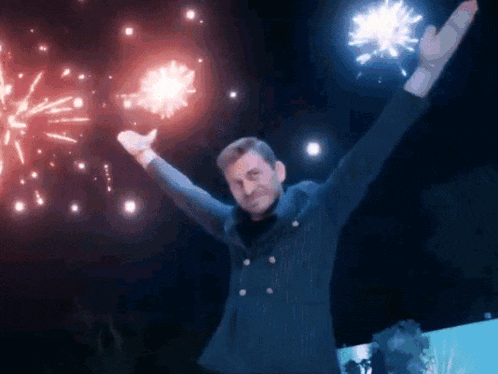 a man in a suit is standing in front of fireworks with his arms in the air