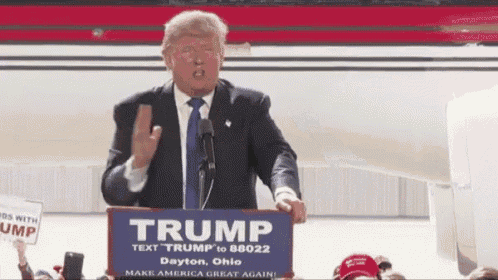 donald trump is giving a speech at a podium holding a sign that says trump