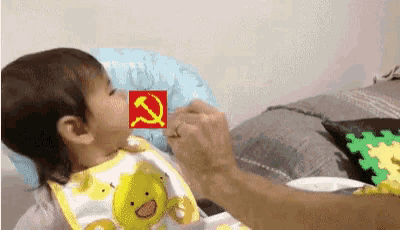 a baby is being fed with a spoon with a hammer and sickle on it 's face .