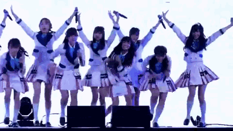 a group of girls are standing on a stage with their hands in the air