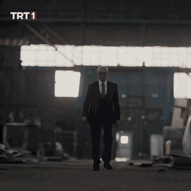 a man in a suit and tie is walking in a dark room with trt 1 written on the bottom