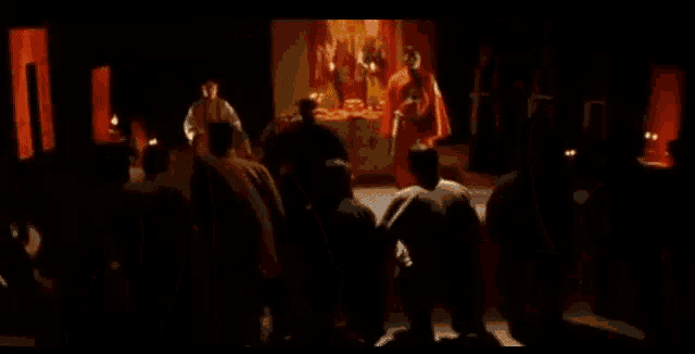 a man in a red robe is talking to another man in front of a crowd of people .