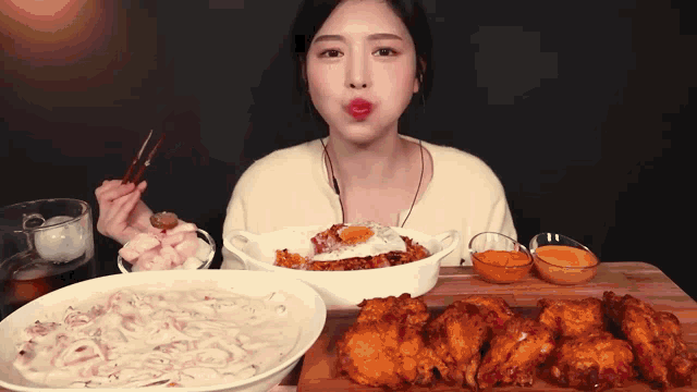 a woman eating a bowl of food with chopsticks and a bowl of fried chicken