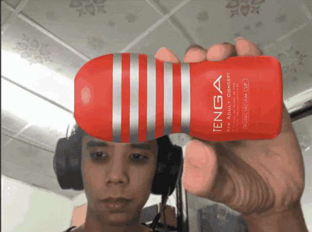 a man wearing headphones is holding a red tenga bottle
