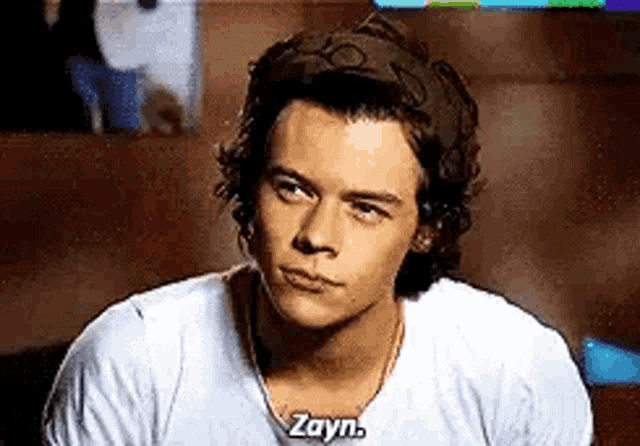 a young man wearing a headband and a white shirt is talking to zayn .