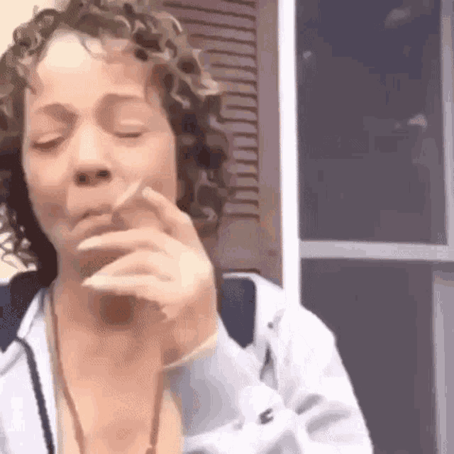 a woman is smoking a cigarette in front of a window with her eyes closed .