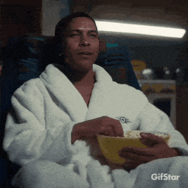 a man in a bathrobe is eating popcorn from a bowl