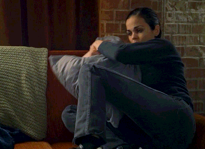 a woman sitting on a couch hugging a pillow with a brick wall behind her