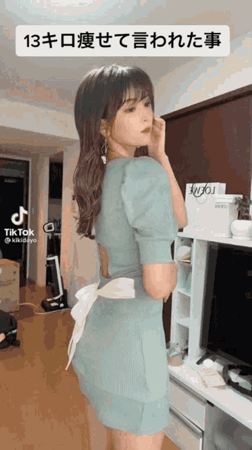 a woman in a blue dress is standing in front of a tv and a sign that says tik tok