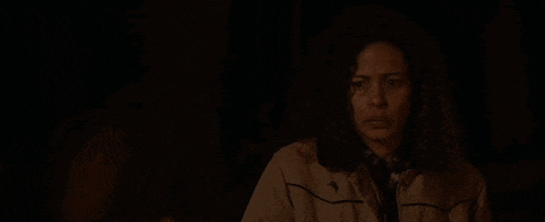 a woman with curly hair is looking at the camera in the dark .