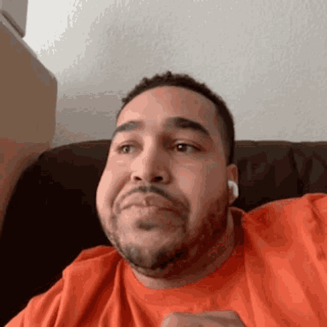 a man with a beard and ear buds is sitting on a couch .