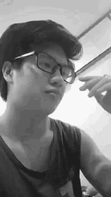 a young man wearing glasses and a tank top is making a funny face .