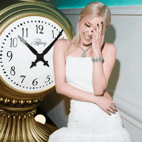 a woman in a white dress stands in front of a gold tiffany clock