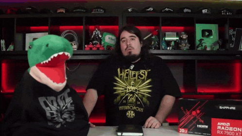 a man wearing a shirt that says hellfest is talking to a stuffed dinosaur