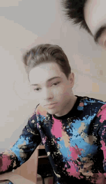 a young man wearing a colorful shirt is sitting at a table