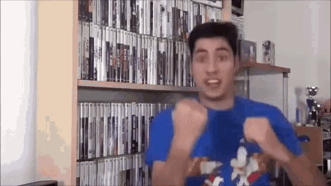 a man wearing a sonic the hedgehog shirt is standing in front of a shelf full of dvds .