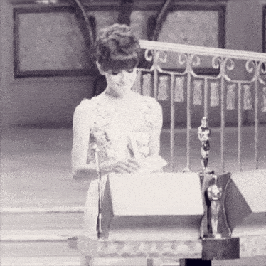 a woman in a white dress is standing in front of a podium with an oscar statue in the background