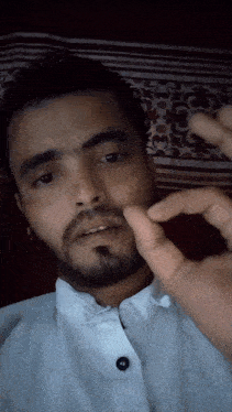 a man with a beard wearing a white shirt holds his finger to his mouth