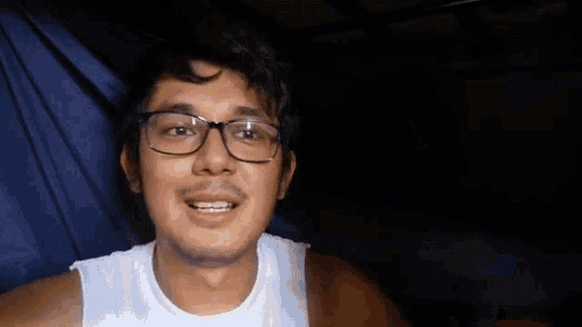 a man wearing glasses and a white shirt is giving a thumbs up .