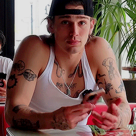 a man with a lot of tattoos on his arms is sitting at a table