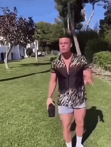 a man in a zebra print shirt and shorts is standing in a grassy area