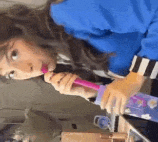 a woman is brushing her teeth with a pink toothbrush and a purple bottle .