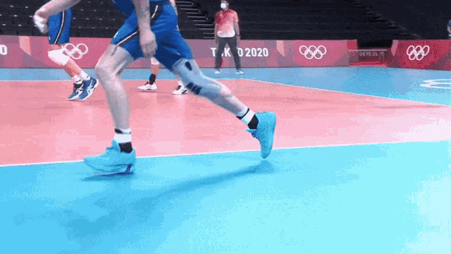 a man in blue shorts is running on a volleyball court in front of a banner that says tokyo 2020