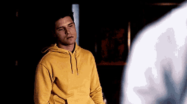 a young man in a yellow hoodie is standing in a dark room .