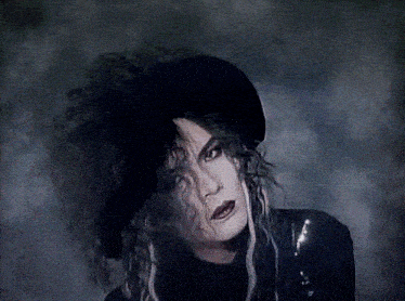 a woman wearing a black hat and a black jacket is looking at the camera