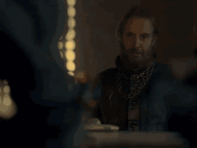 a man with a beard and a chain around his neck is sitting at a table with other people .