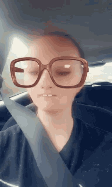a woman wearing glasses is sitting in a car with her eyes closed