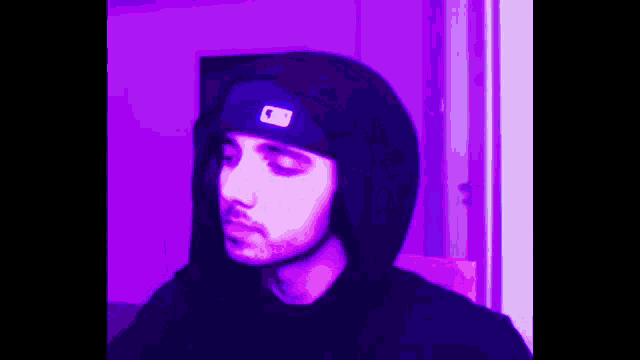 a man wearing a black hoodie and a purple hat is standing in front of a door .
